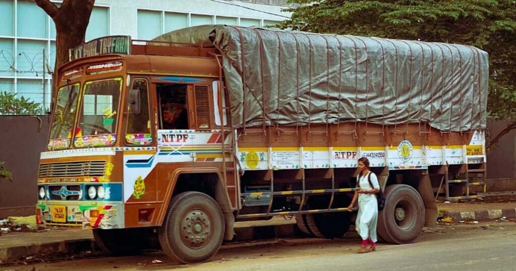 Man standing beside a commercial truck with a tarp-covered trailer